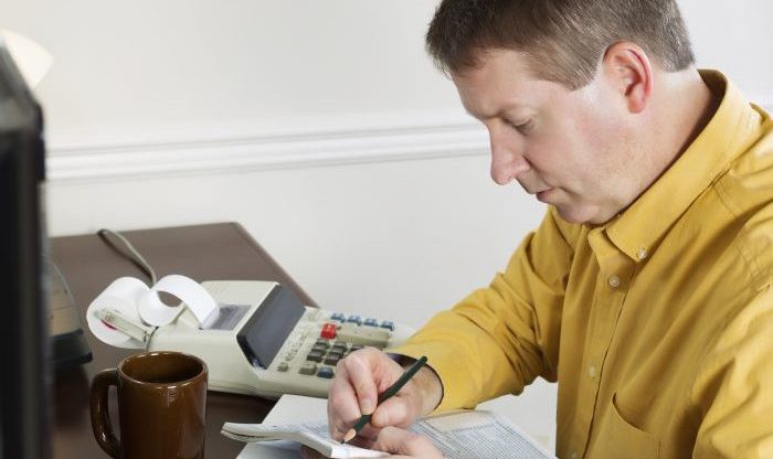 Photo of mature man, recording data from the computer, working on his taxes with tax booklet and pencil in hands
